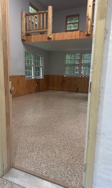 Interior room with a tan flake-coated floor, wood wainscoting and a loft railing