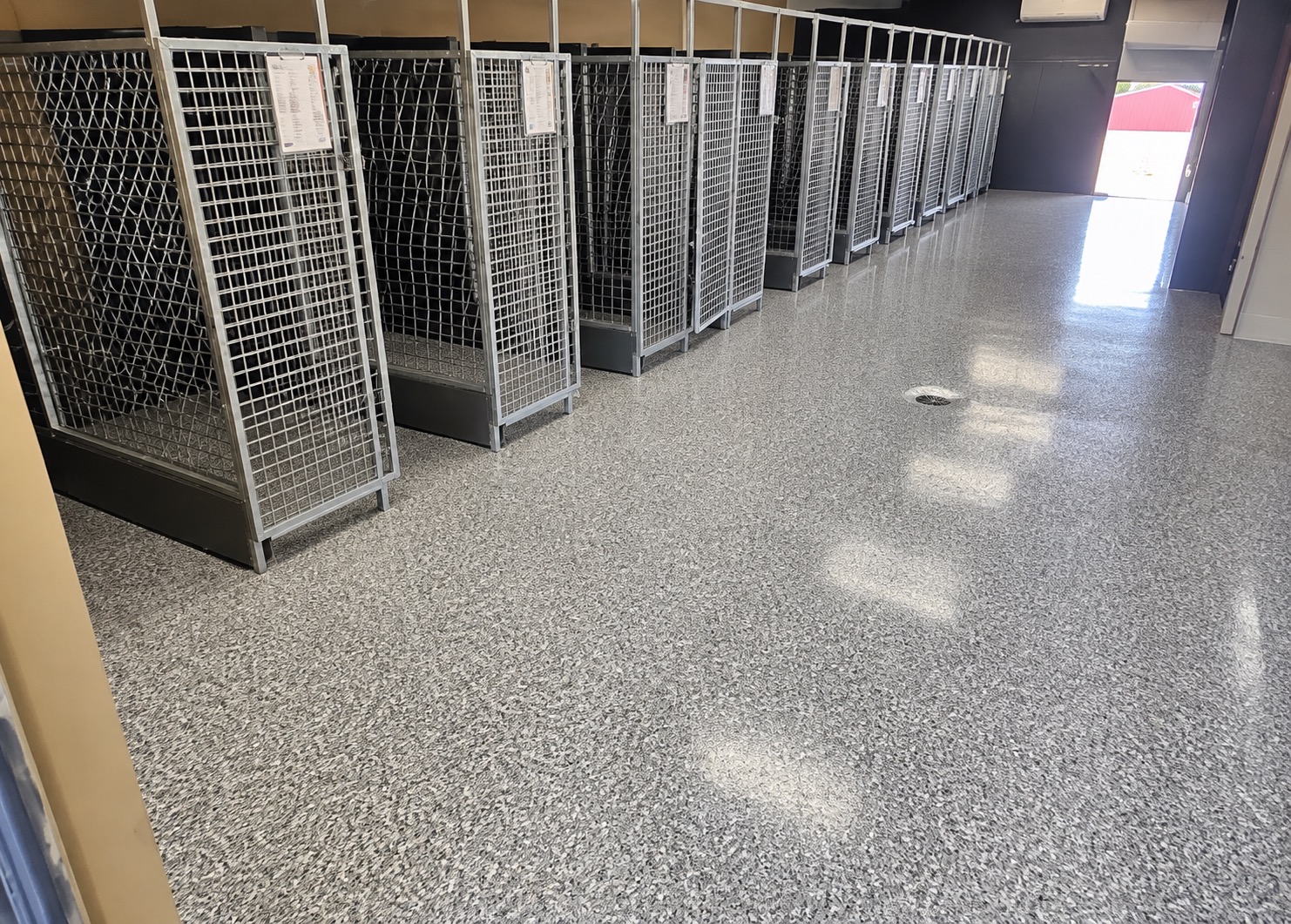 Dog kennel facility with a glossy gray flake floor running the length of a row of wire kennel runs, with a floor drain