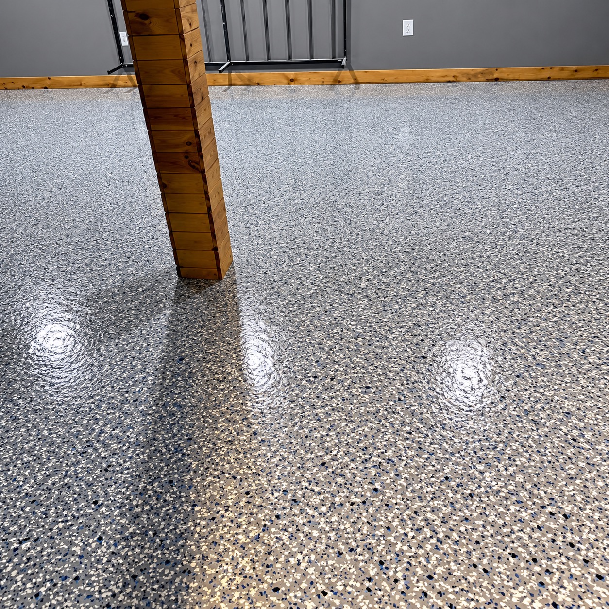 The same basement room after coating: glossy gray flake floor with white, black and blue chips around the wood-clad post