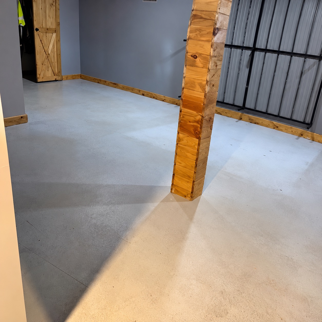 Finished basement room before coating: plain gray concrete floor around a wood-clad support post