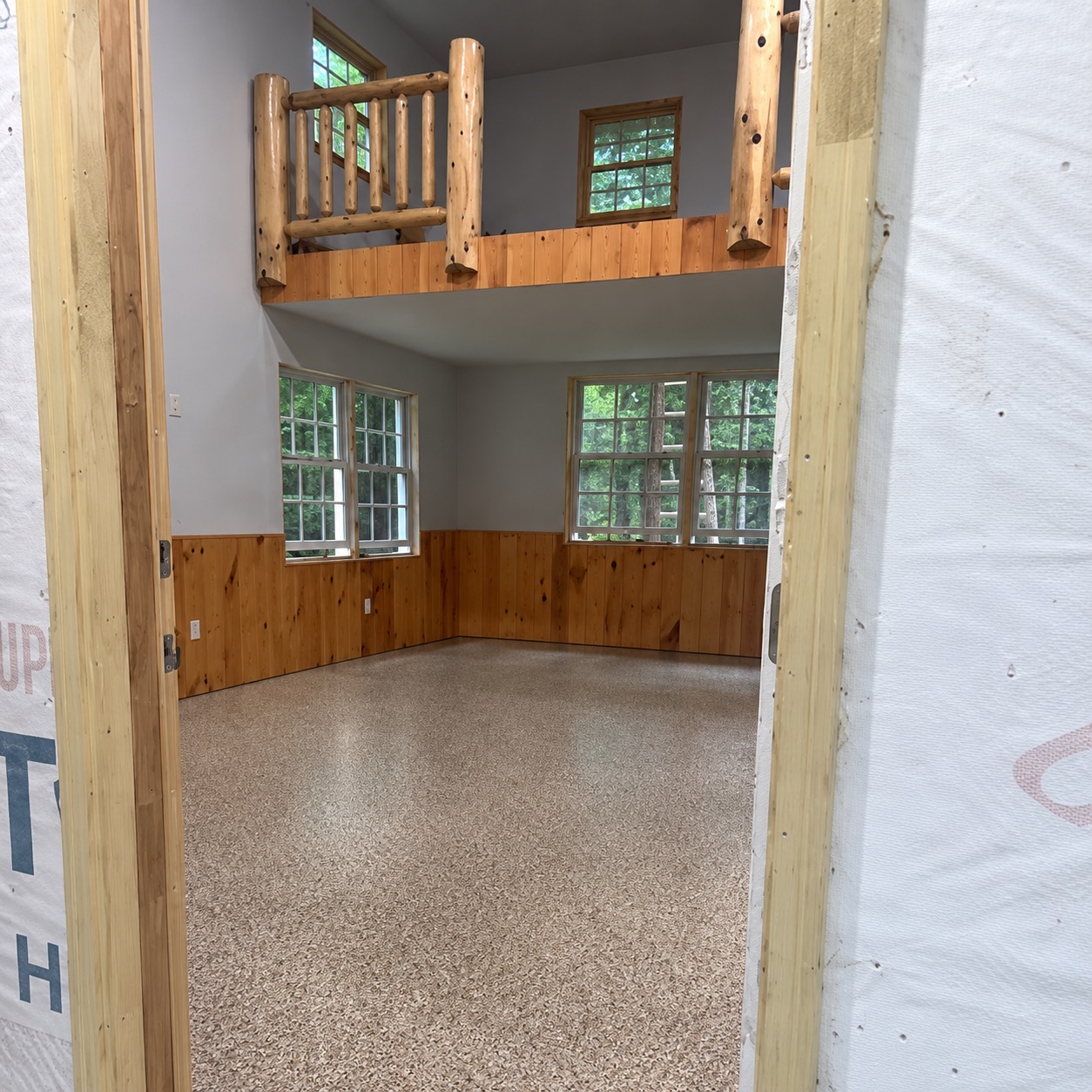The same cabin great room finished: tan flake floor beneath pine wainscoting and the log loft railing